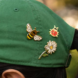 Three pins shaped like a bee, ladybug, and flower on a green cap.