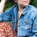 Person wearing a denim jacket with a butterfly pin, standing outdoors.