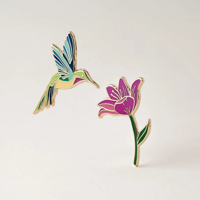 Colorful hummingbird and flower enamel pins on a light gray background