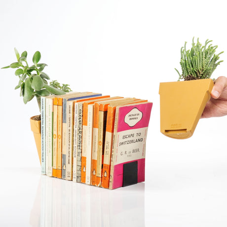 a planter cut in half serving as bookends for a row of books with hand holding one of the bookends, on a white background