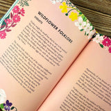 Open book with floral designs and a page titled "Wildflower Folklore: Violets" on a wooden surface