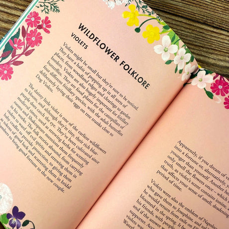 Open book with floral designs and a page titled "Wildflower Folklore: Violets" on a wooden surface