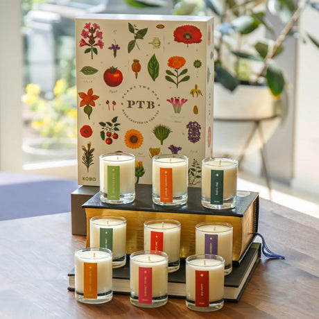 Collection of candles with colorful labels on a wooden surface, featuring a decorative box in the background.