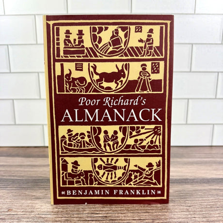 Book titled 'Poor Richard's Almanack' by Benjamin Franklin on a wooden surface with a tiled wall background.