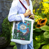 Person holding a tote bag with Old Farmer's Almanac design, surrounded by sunflowers and greenery.