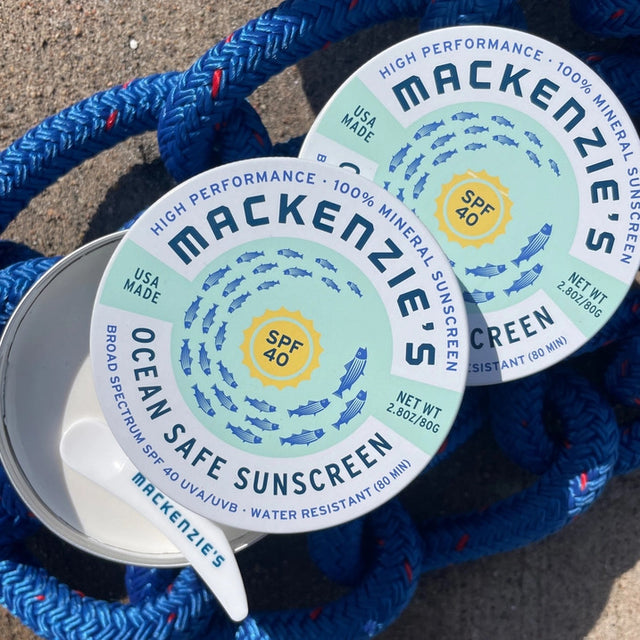 two tins of ocean safe sunscreen on a sandy beach with blue mariner's rope