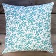 Decorative pillow with teal seaweed pattern on a wooden surface