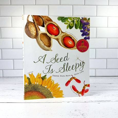 Book titled 'A Seed Is Sleepy' with illustrations of a sunflower and seeds on a white background.