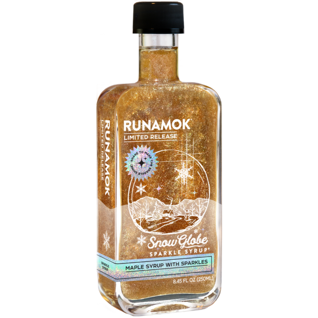snow globe sparkle syrup bottle showing the charming winter themed label featuring a round globe with a snowy landscape with a cozy cabin surrounded by trees and snowflakes
