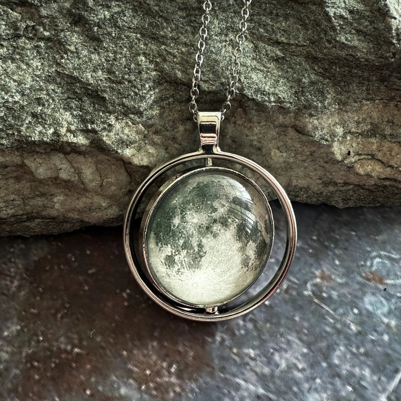 Silver necklace with a round pendant featuring a moon design, against a stone background.
