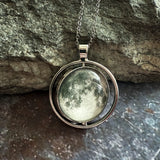 Silver necklace with a round pendant featuring a moon design, against a stone background.