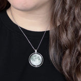 Person wearing a necklace with a moon-phase pendant on a black shirt