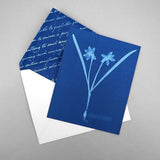 Blue greeting card with floral design and white envelope with blue interior on gray background