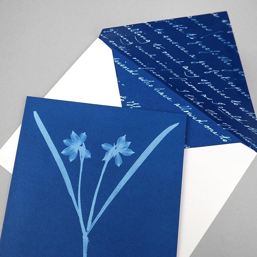 Blue greeting card with floral design and an white envelope folded open to reveal blue interior of the envelope with white cursive writing