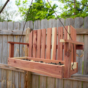 the cedar swing bird feeder hanging from a tree in a backyard with a wooden fence in the background