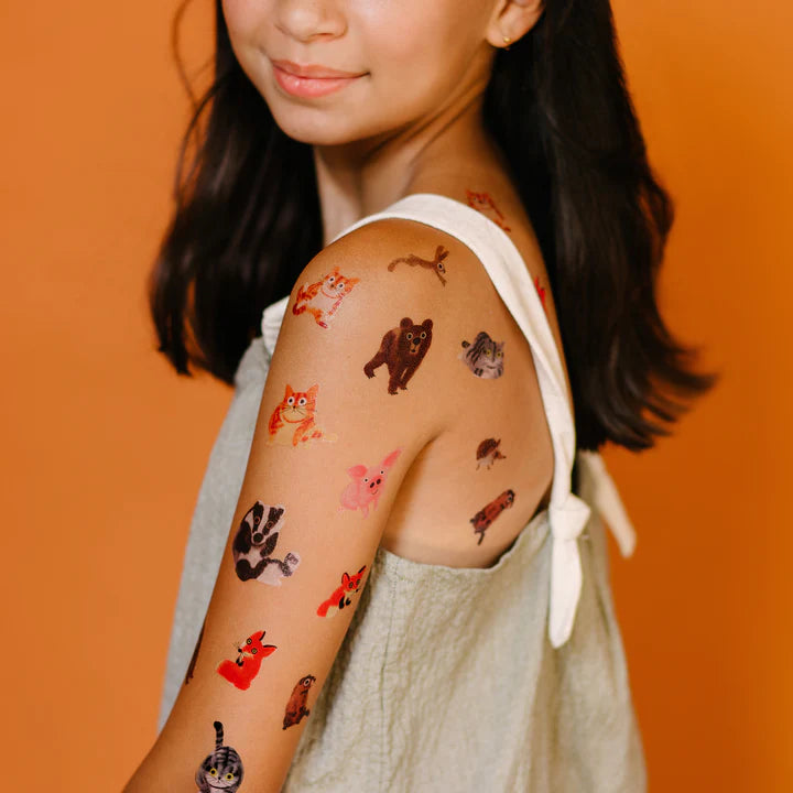 Young girl with temporary tattoos of animals on her arm against an orange background