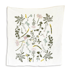 an off white tea towel with colorful botanical illustrations of edible wild foods including clover, herbs, asparagus, and more