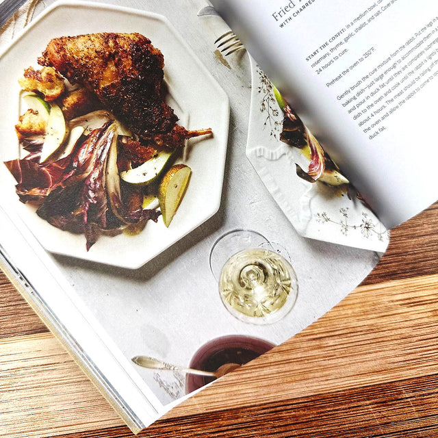Fried dish with vegetables on a plate, glass of white wine, and book open to a recipe page.