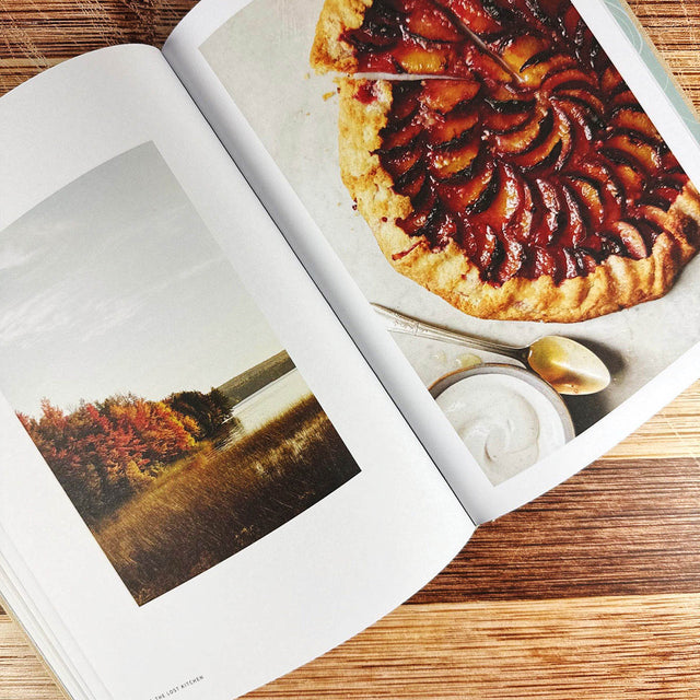 Open book showing a photo of a dessert and a scenic landscape on a wooden surface