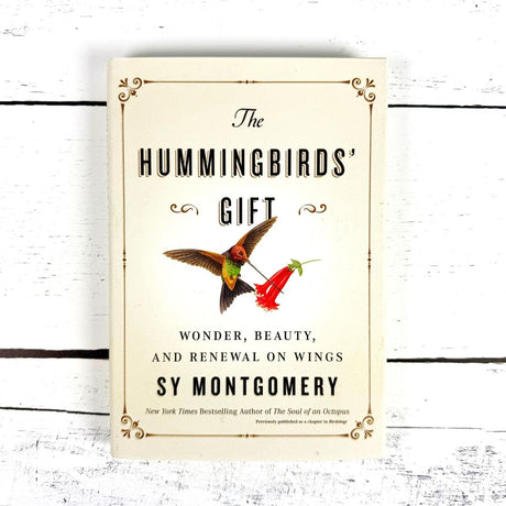Book cover of 'The Hummingbirds' Gift' by Sy Montgomery on a white wooden background