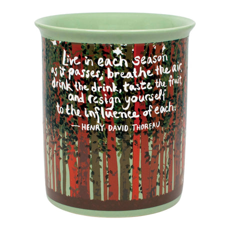 A ceramic cup featuring a forest design with red and green trees and a quote by Henry David Thoreau printed on the side, set against a plain white background.