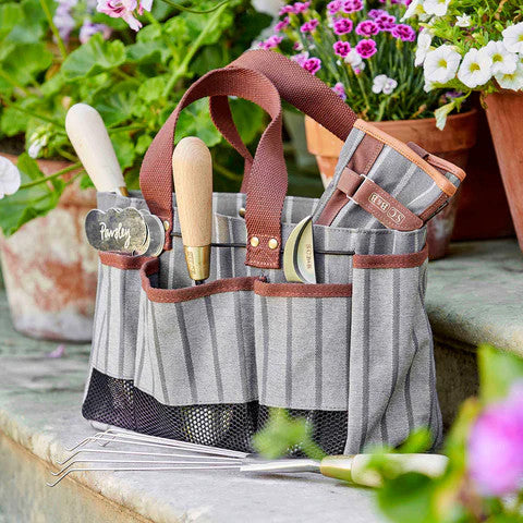 The tool bag filled with gardening tools in its various pockets sitting on stone steps in a garden 
