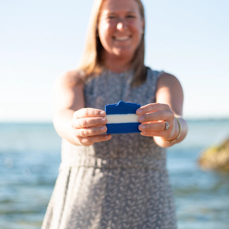 Atlatntic Soap Co founder holding a bar of Ultramarine bar soap with the sea behind her