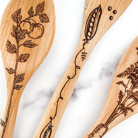 close up of Wooden spoons with engraved vegetable designs on a marble surface