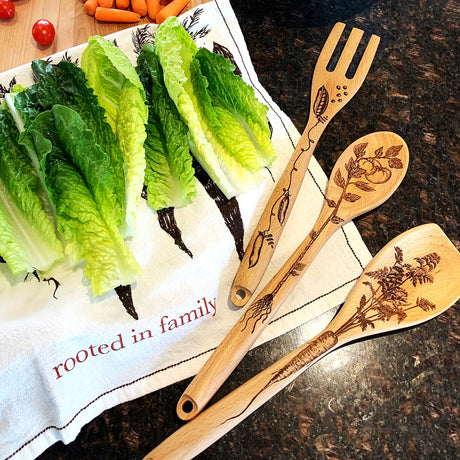 Wooden utensils with engraved designs on a kitchen towel with 'rooted in family' text.