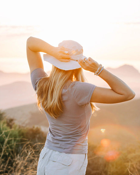 a model wearing the Venture sun hat with their back to the viewer and hands at the back of their head about to pull their hair through the ponytail hole in the back of the hat