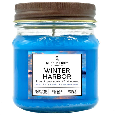 a candle in a clear glass mason jar with off blue and a label that reads "Winter Harbor" against a white background