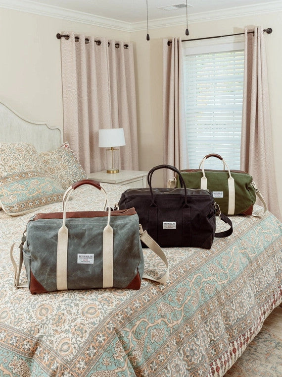a hotel room bed with the 2 weekender bags lined up on it