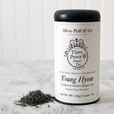 a tin of Oliver Pluff & Co Young Hyson loose tea with white label and colonial era tea tax stamp art on the package and small heap of loose tea next to the package on a marble surface with white background