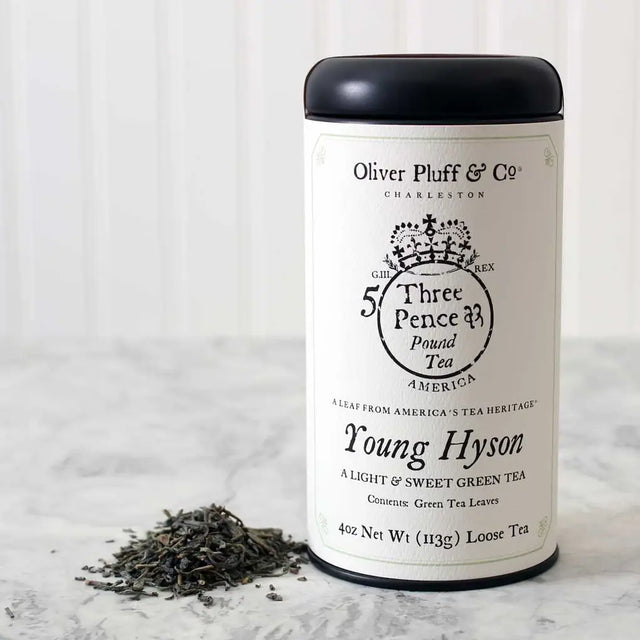 a tin of Oliver Pluff & Co Young Hyson loose tea with white label and colonial era tea tax stamp art on the package and small heap of loose tea next to the package on a marble surface with white background