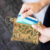 Person holding a small floral-patterned cork wallet with a card in it.