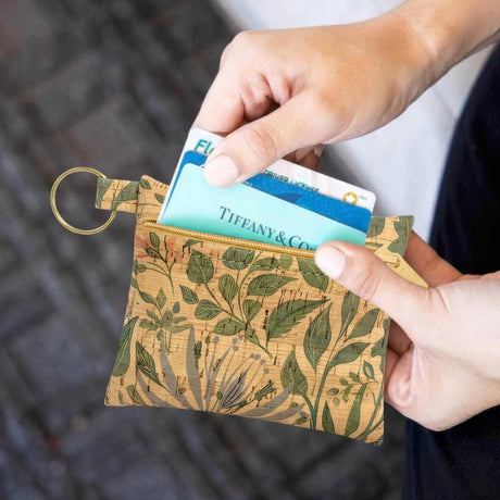 Person holding a small floral-patterned cork wallet with a card in it.