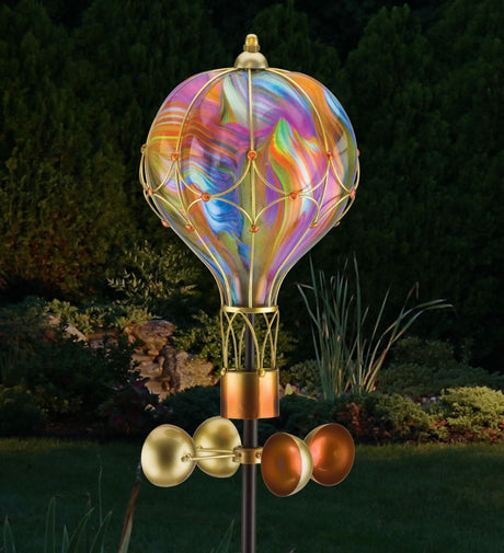 Orange swirl balloon spinner solar stake lit up in a garden at night. A warm, colorful glow is emitted from the balloon