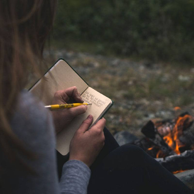a closeup of a woman by a fire writing in her notebook