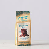 A bag of Ragged Coast Craft Chocolate Brownie Mix, featuring a kraft paper packaging with teal decorative accents and a central white label showing a chocolate brownie stack.