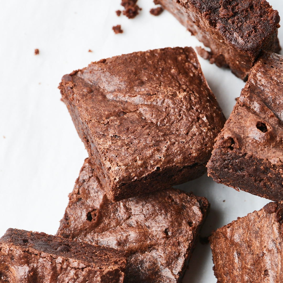 Several glossy chocolate brownies arranged on a white surface, with a few crumbs scattered nearby.