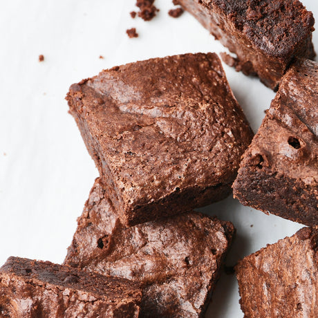 Several glossy chocolate brownies arranged on a white surface, with a few crumbs scattered nearby.