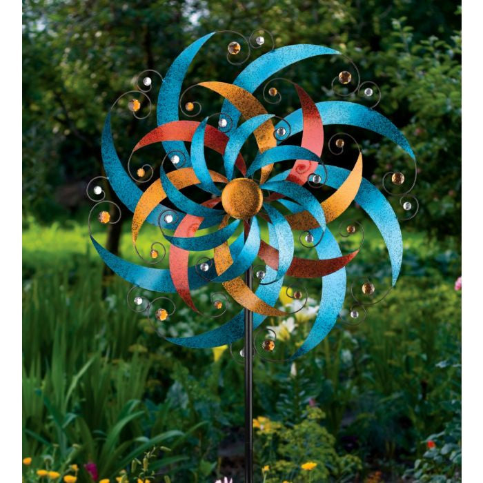 The Crescent Wind Spinner displayed in a garden, showcasing its vibrant colors and sparkling gems, adding a dynamic and decorative touch to the outdoor space