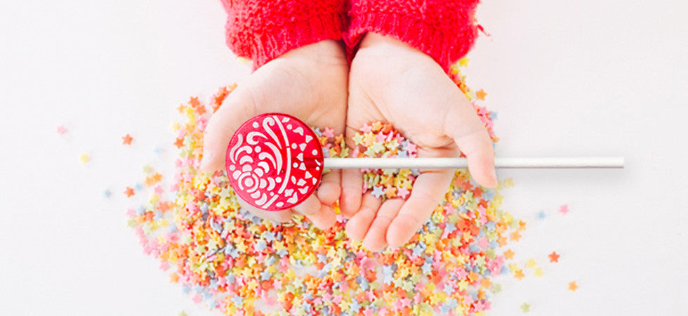 a pair of hands cupping  colorful star shaped sprinkles and a bright red lollipop
