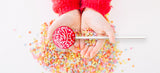 a pair of hands cupping  colorful star shaped sprinkles and a bright red lollipop