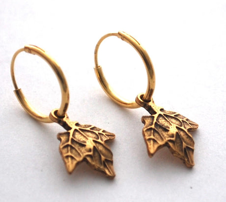 close up of gold maple hoop earrings on a white surface
