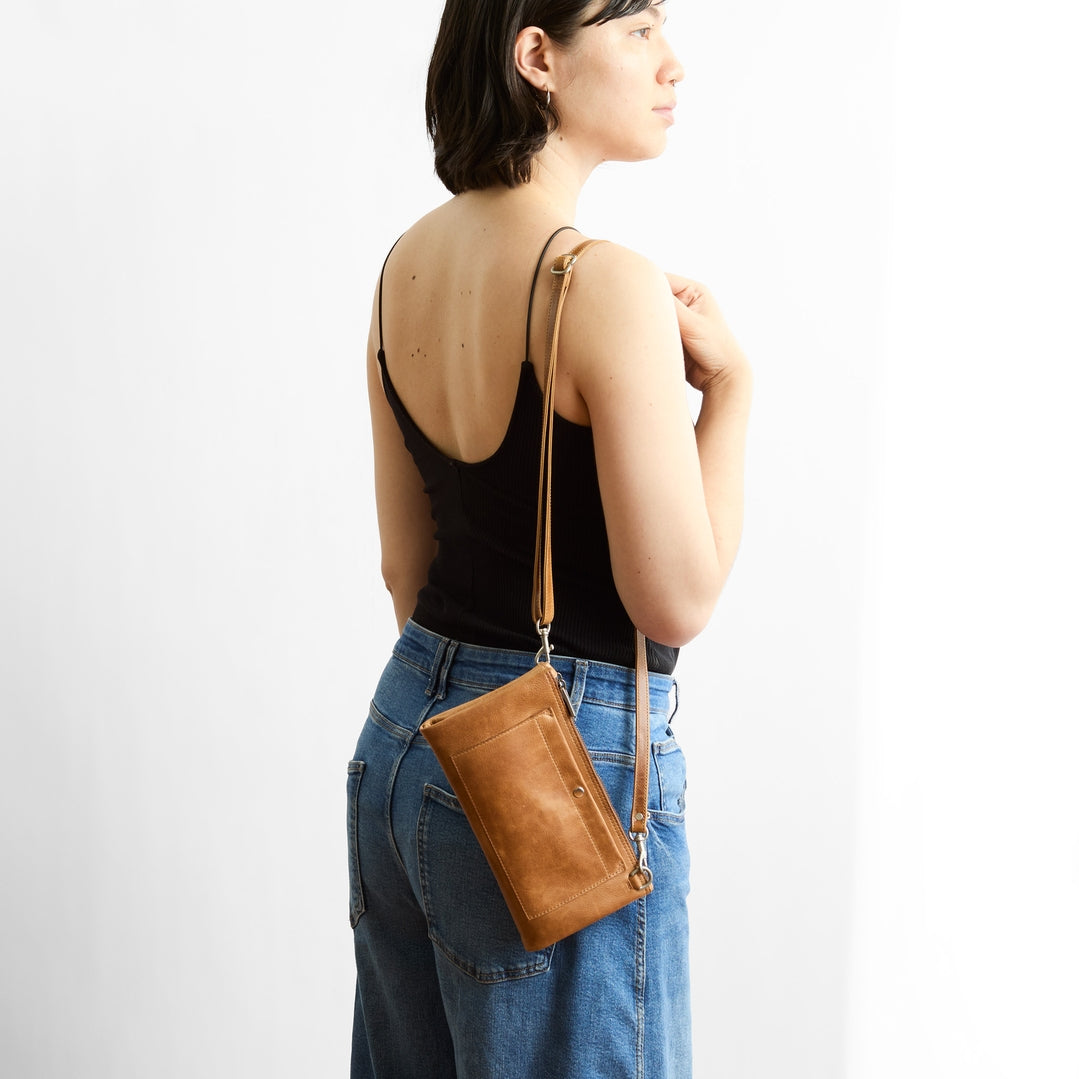 Person wearing a black top and blue jeans with a brown leather crossbody bag on a white background