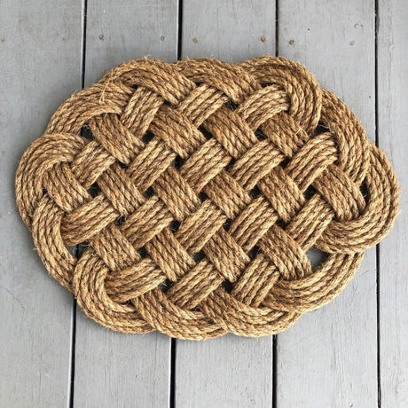 a hand woven rounded nautical door mat with intricate pattern on a gray wooden dock