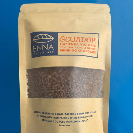 a kraft colored sealed pouch with a window making the chocolate in the package visible - text on the bag reads "Enna Chocolate - Ecuador Hacienda Victoria - 76% Dark - Single Origin Drinking Chocolate - Crafted by hand in small batches from bean to bar in Exeter, New Hampshire with single origin ethically sourced heirloom cacao - 6 ounces."