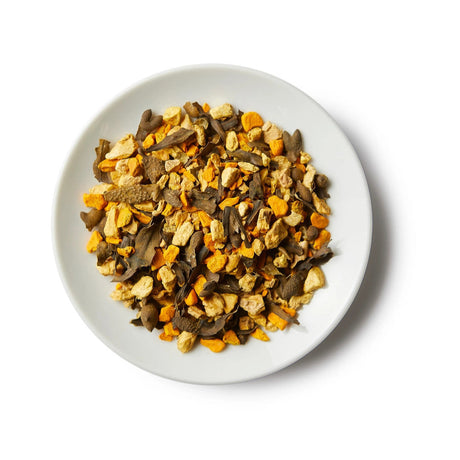 a small white round dish containing a mound of sailor's cure all loose leaf tea showing the strong yellow turmeric ingredients, seaweed, and others