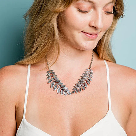 Woman wearing a silver leaf necklace against a light blue background